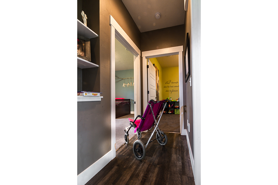 Wide hallways, with black-stained wood, allow for a comfortable area of travel inside the home. A pink stroller sits, turned to enter a widened doorway into a room.